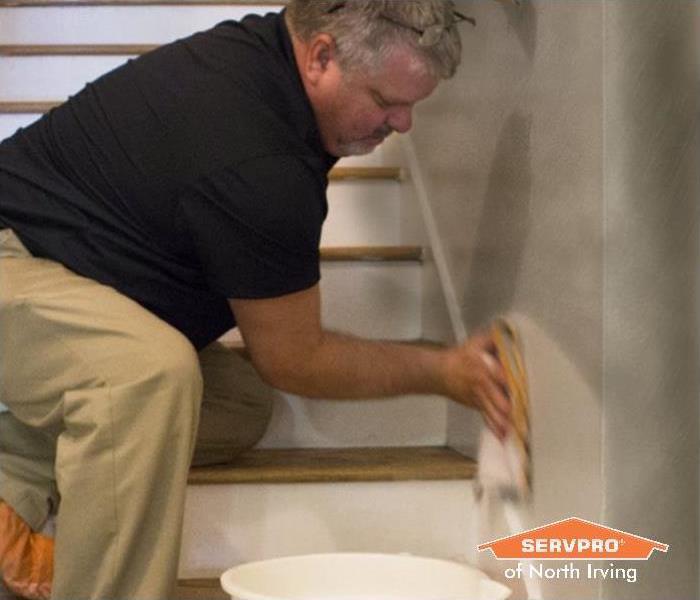man in a black shirt, khaki pants, and orange shoe covers cleans a soot damaged wall